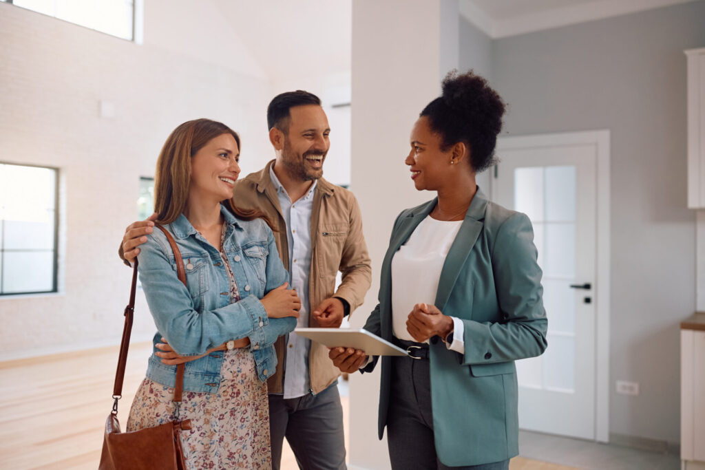 African American real estate agent using touchpad while talking to happy couple who is buying new house.