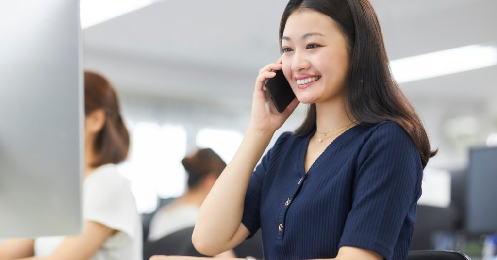 Femme asiatique travaillant sur son ordinateur en souriant, en passant un coup de téléphone